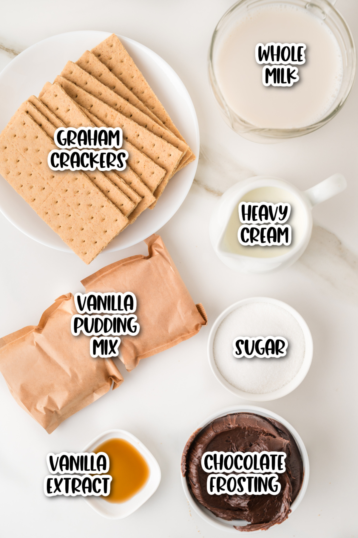 Top-down view of ingredients on a white surface, including graham crackers, whole milk, heavy cream, sugar, vanilla pudding mix, vanilla extract, and chocolate frosting.