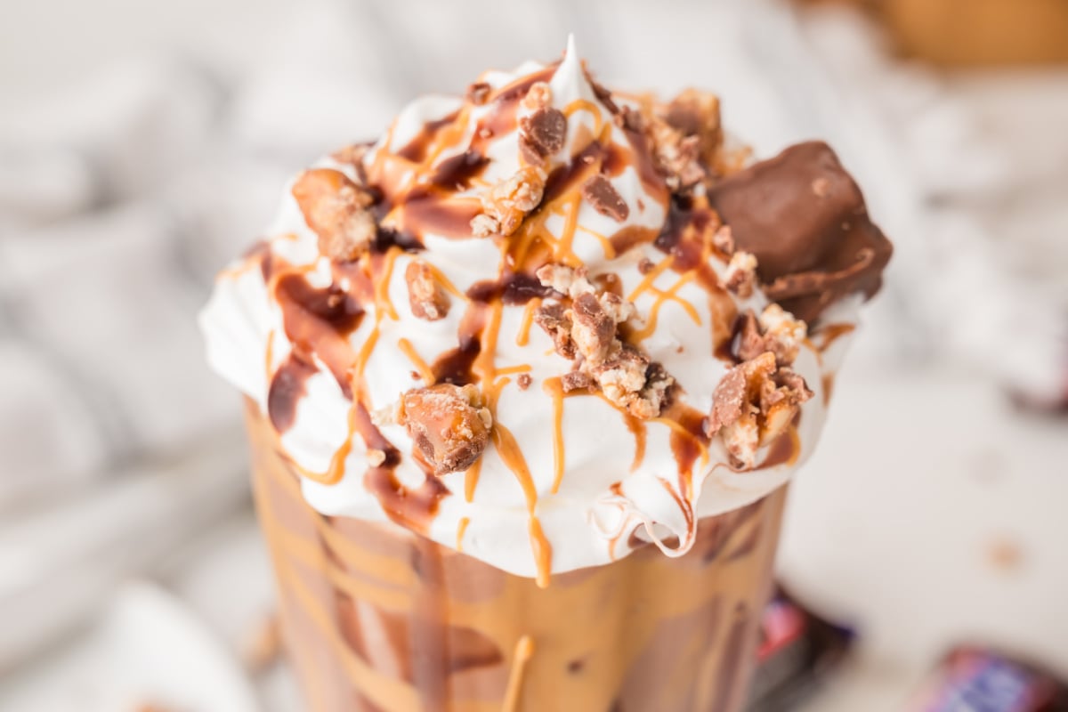 A glass of iced coffee topped with whipped cream, caramel and chocolate drizzle, and pieces of chocolate candy.
