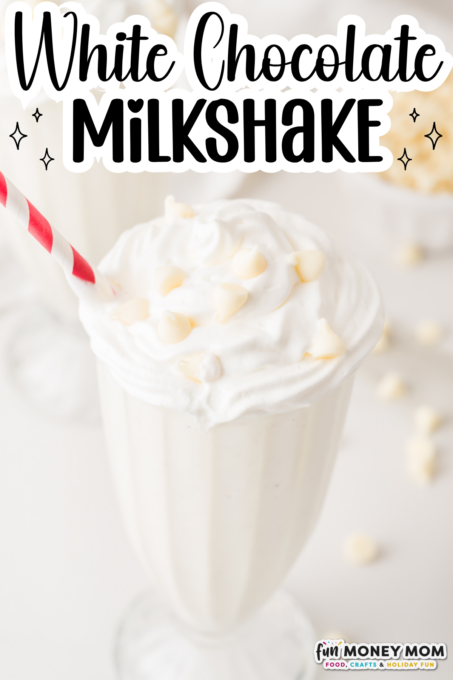 A glass of white chocolate milkshake topped with whipped cream and white chocolate chips, with a red-striped straw.