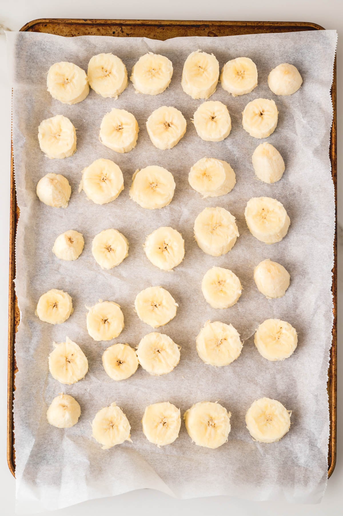 Sliced bananas arranged in rows on a parchment-lined baking sheet.