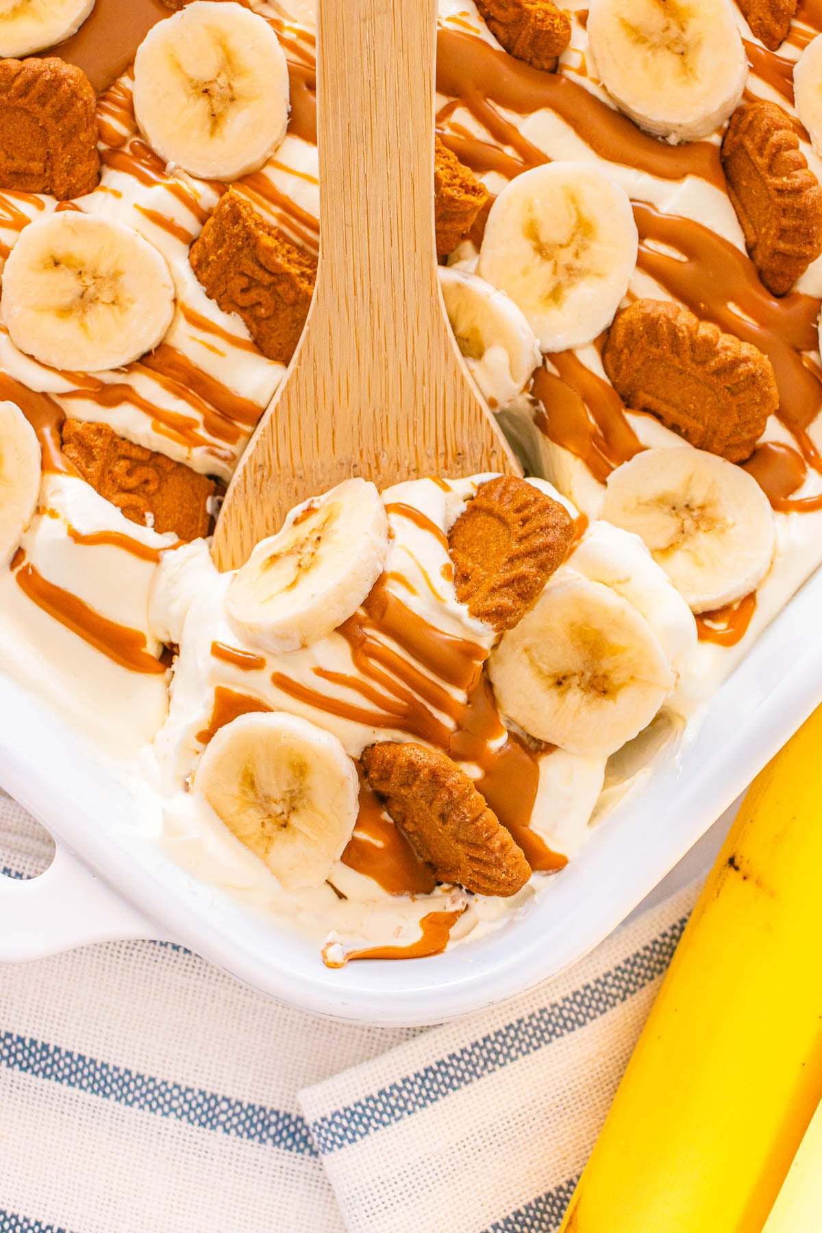 A white dish filled with Biscoff banana pudding, with a wooden spoon.