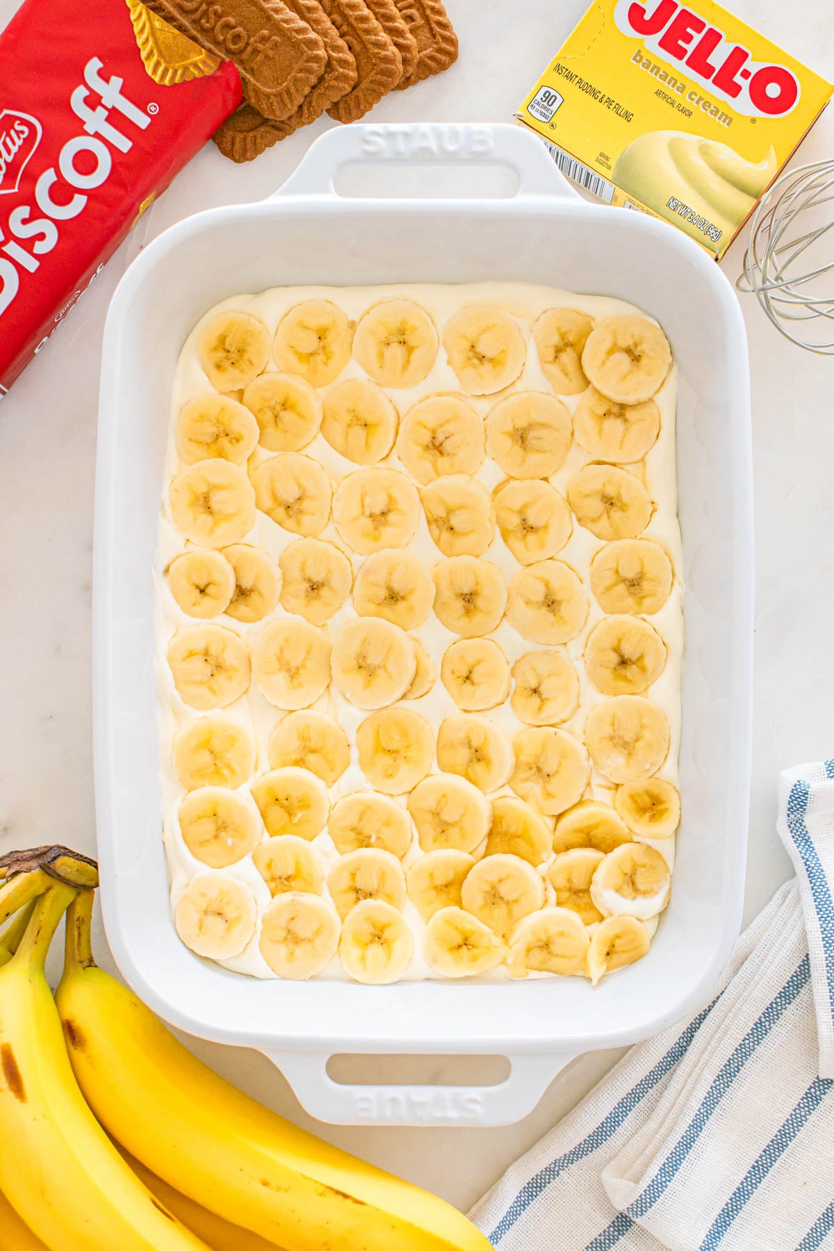 A white baking dish filled with banana cream pudding and topped with sliced bananas.