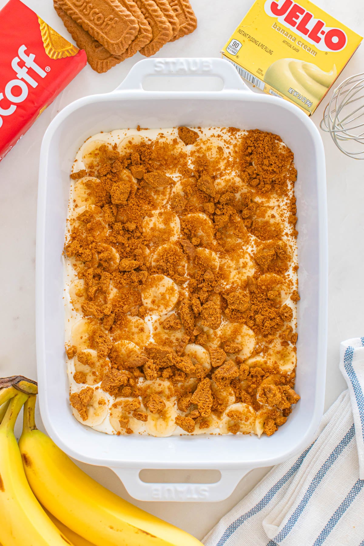 A white baking dish filled with banana cream pudding, sliced bananas, and crushed cookies.