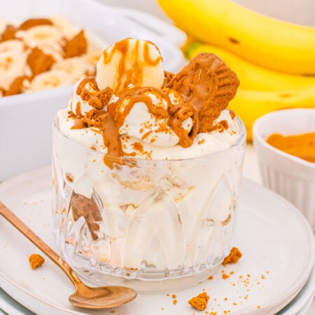 A clear glass bowl filled with Biscoff banana pudding, topped with Biscoff cookies, and cookie crumbs.