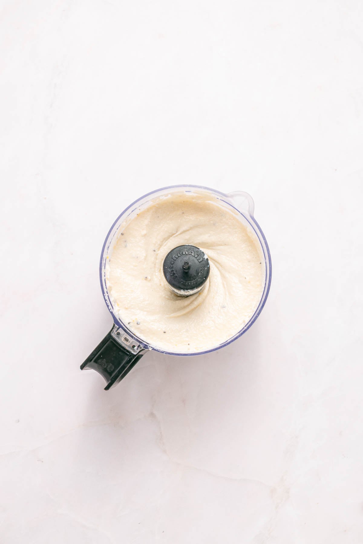 Overhead view of a food processor containing a smooth, creamy mixture on a light-colored surface.