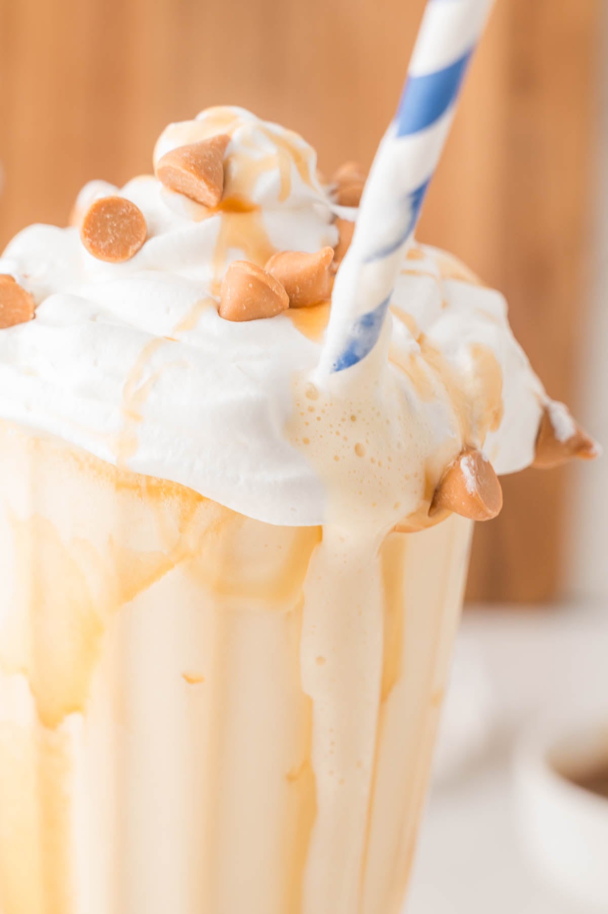 A close-up of a creamy milkshake topped with whipped cream, caramel drizzle, butterscotch chips, and a blue-striped straw.