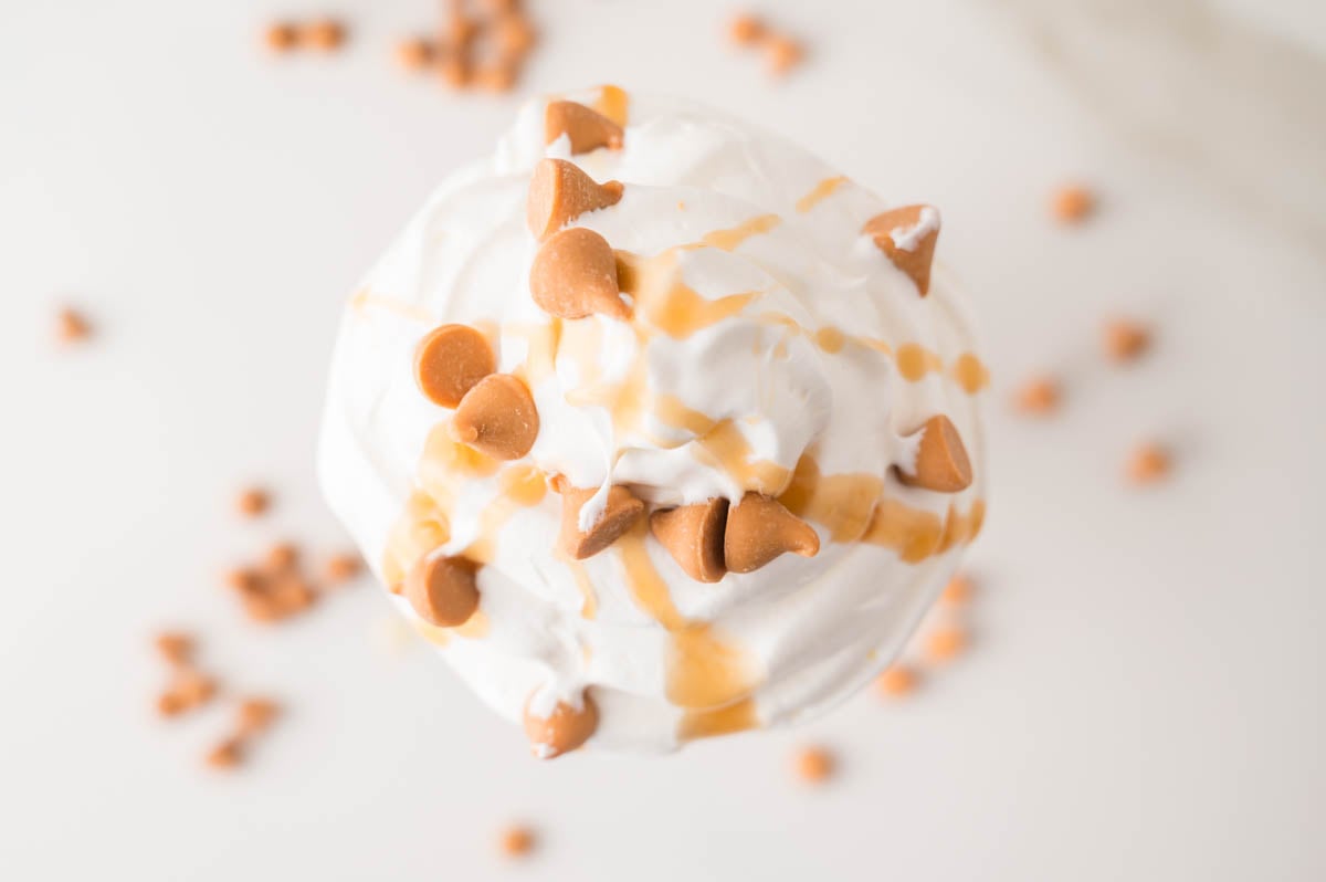 A swirl of whipped cream topped with caramel sauce and butterscotch chips, photographed from above with scattered chips in the background.