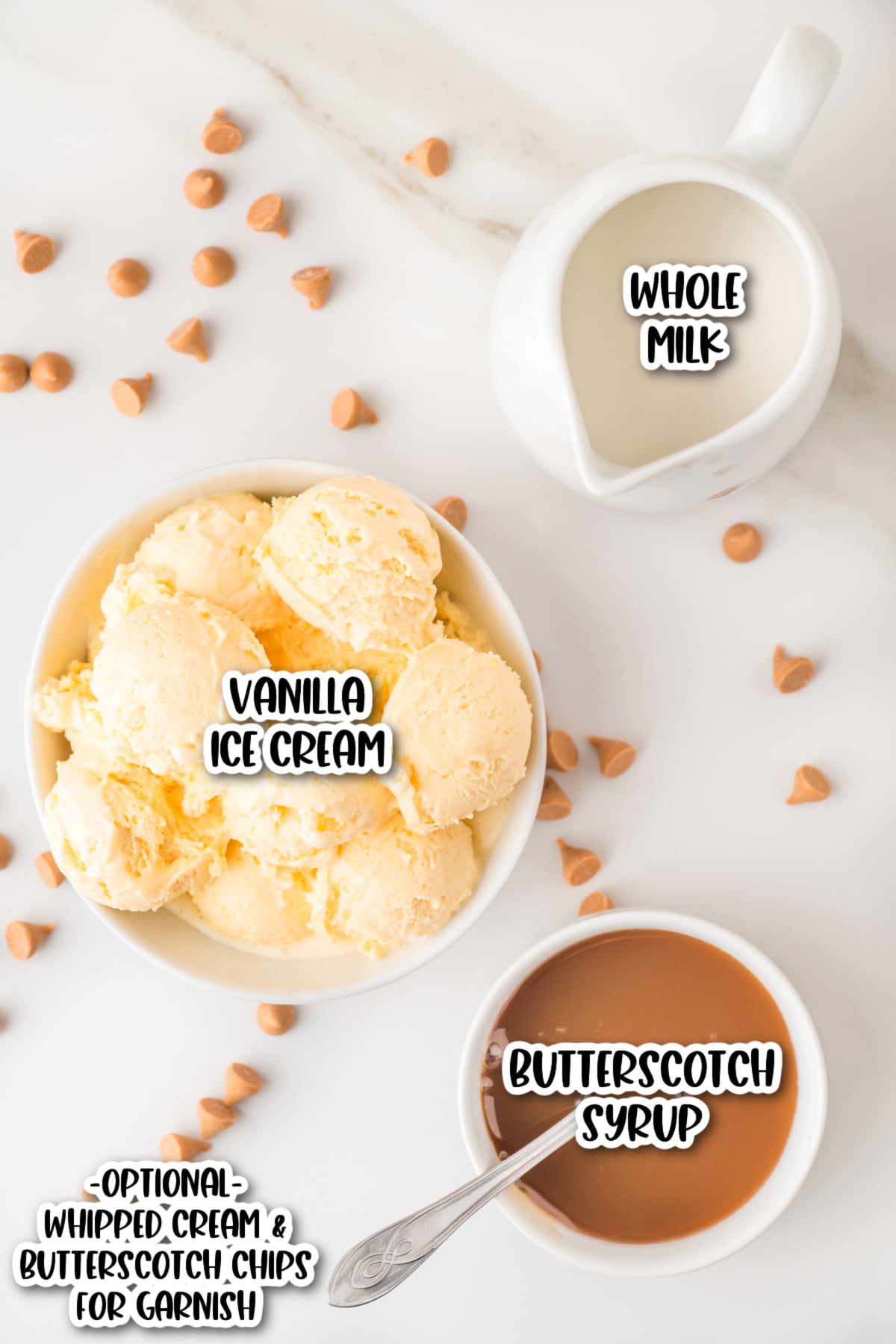 Bowl of vanilla ice cream, a jug of whole milk, a bowl of butterscotch syrup, and scattered butterscotch chips on a white surface.