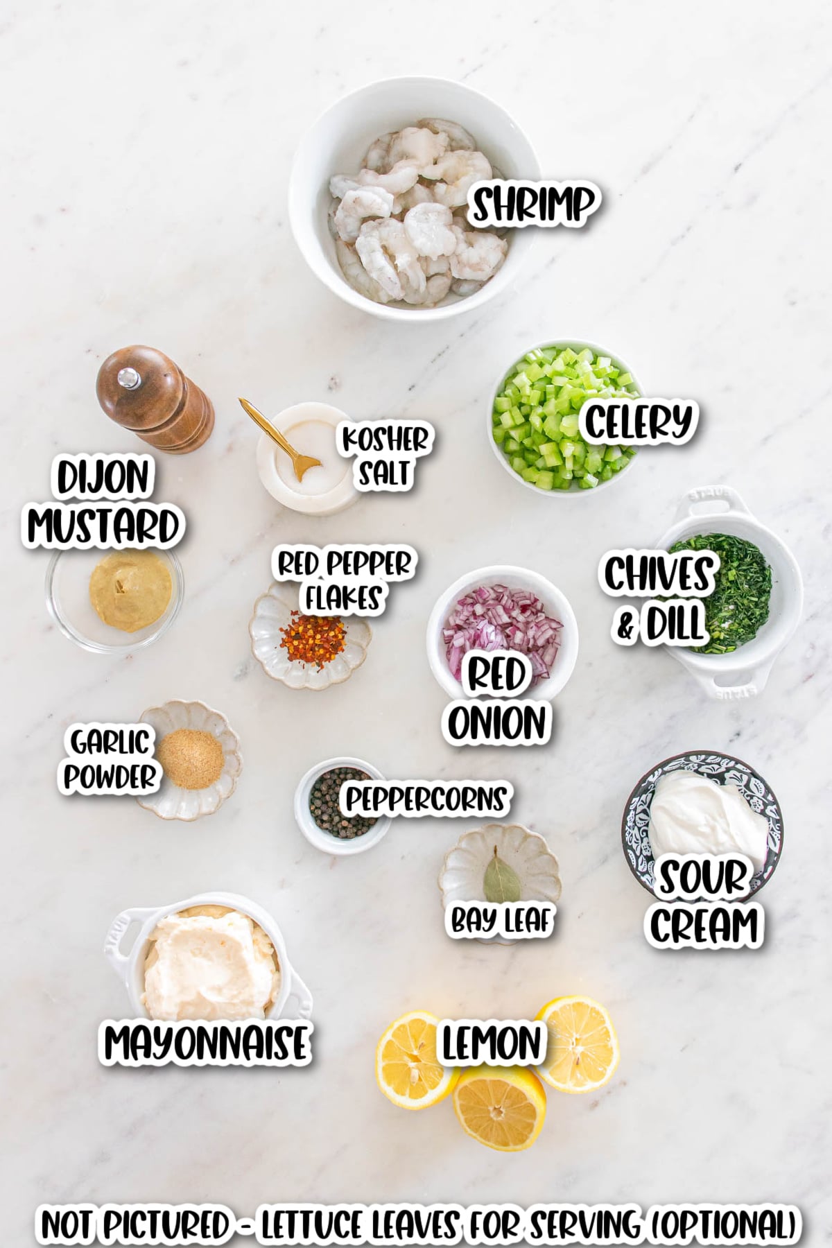 Ingredients for a shrimp salad displayed on a white surface, including shrimp, celery, red onion, chives, dill, sour cream, mayonnaise, lemon, and seasonings.