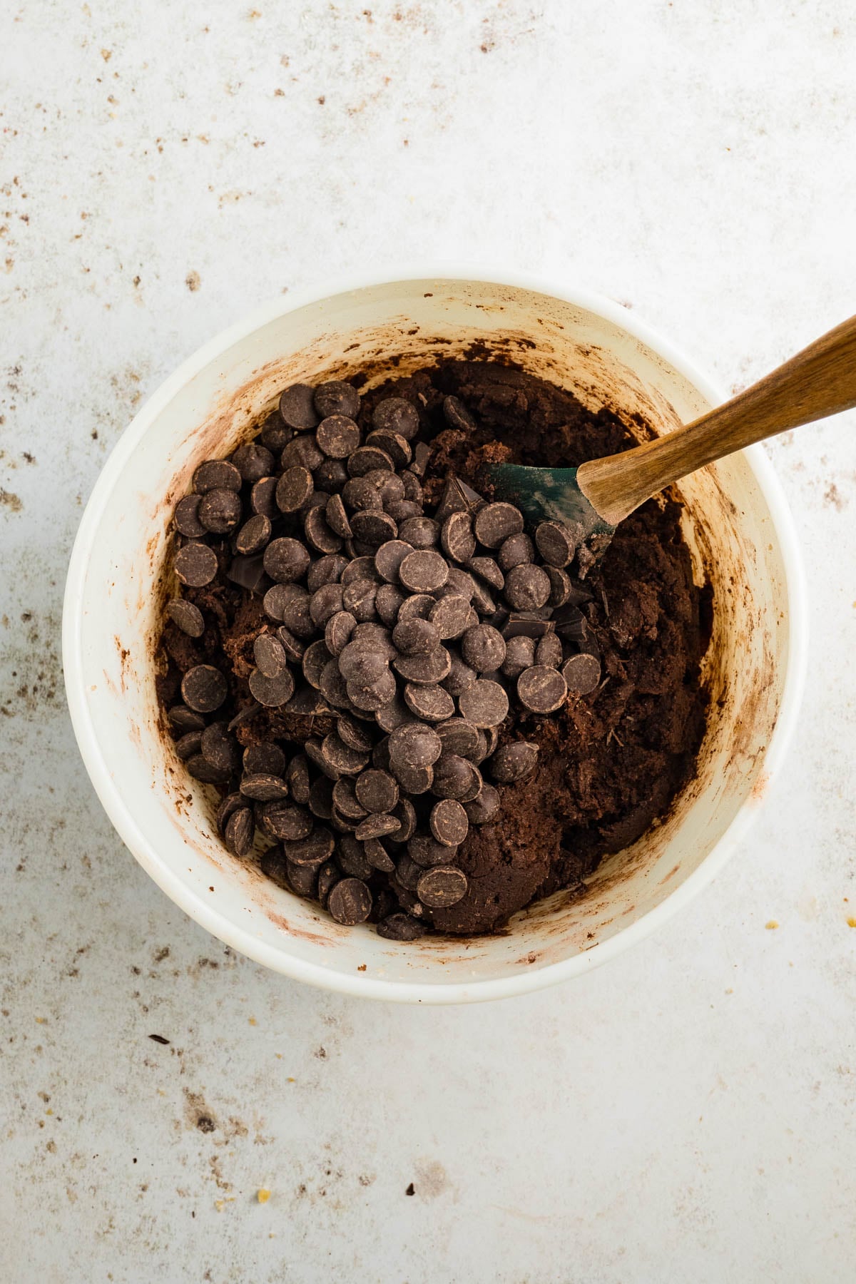 A mixing bowl filled with chocolate cookie dough and chocolate chips being stirred with a spatula.