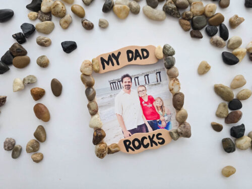 Framed photo saying "My Dad Rocks" decorated with small stones, showing a man, woman, and child standing on a beach with a pier in the background.