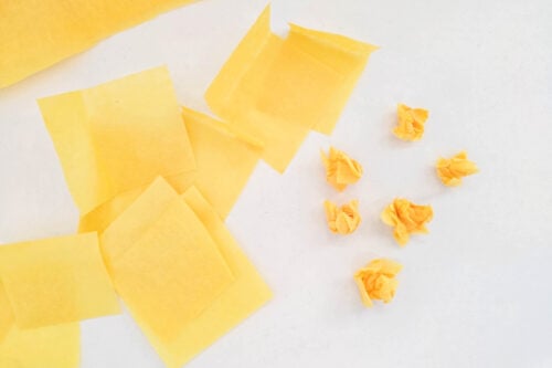 Several yellow tissue paper squares and small crumpled paper balls are arranged on a white surface.