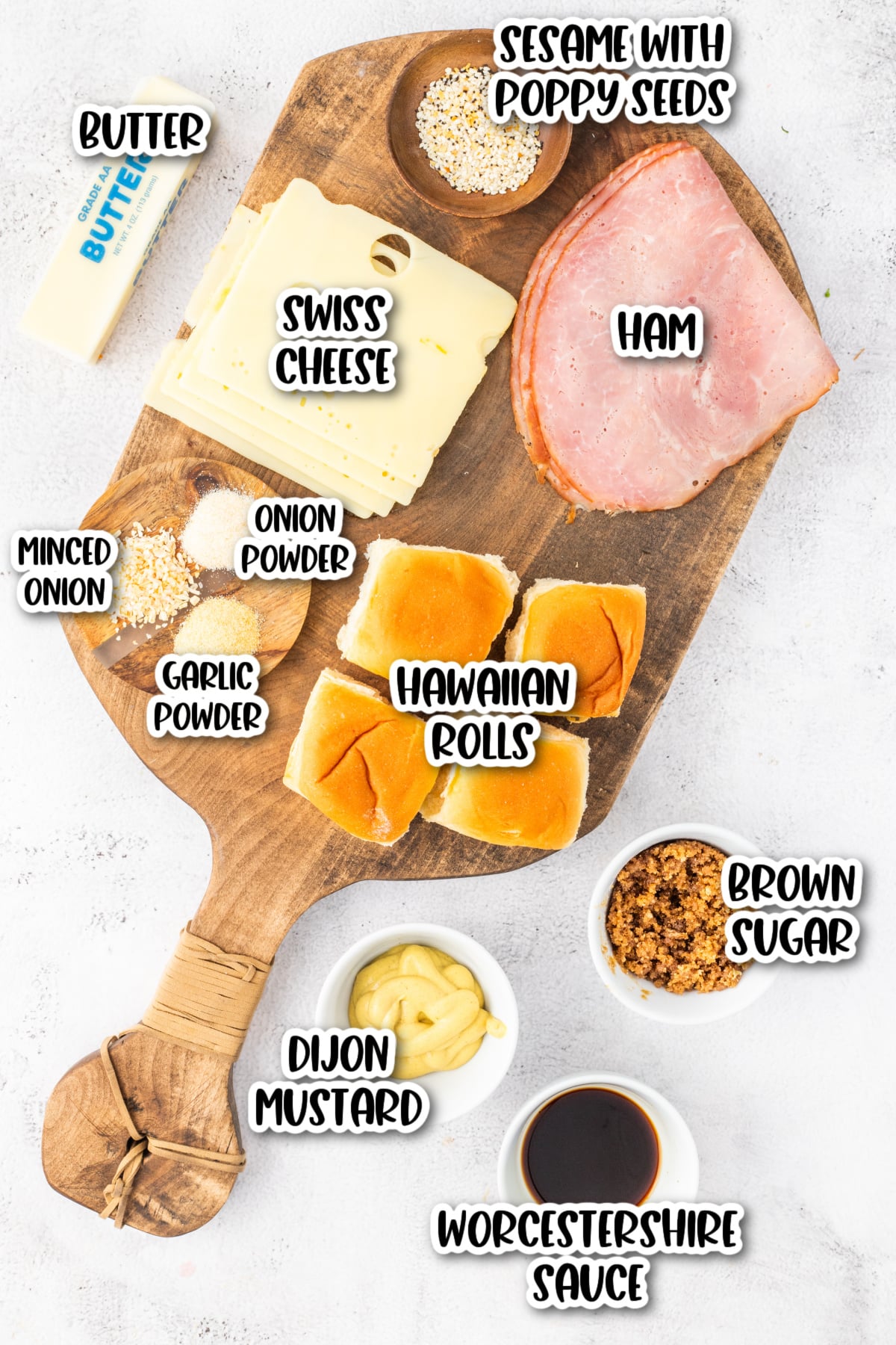 A wooden board with ham, Swiss cheese, Hawaiian rolls, butter, poppy seeds, minced onion, garlic powder, onion powder, Dijon mustard, brown sugar, and Worcestershire sauce.