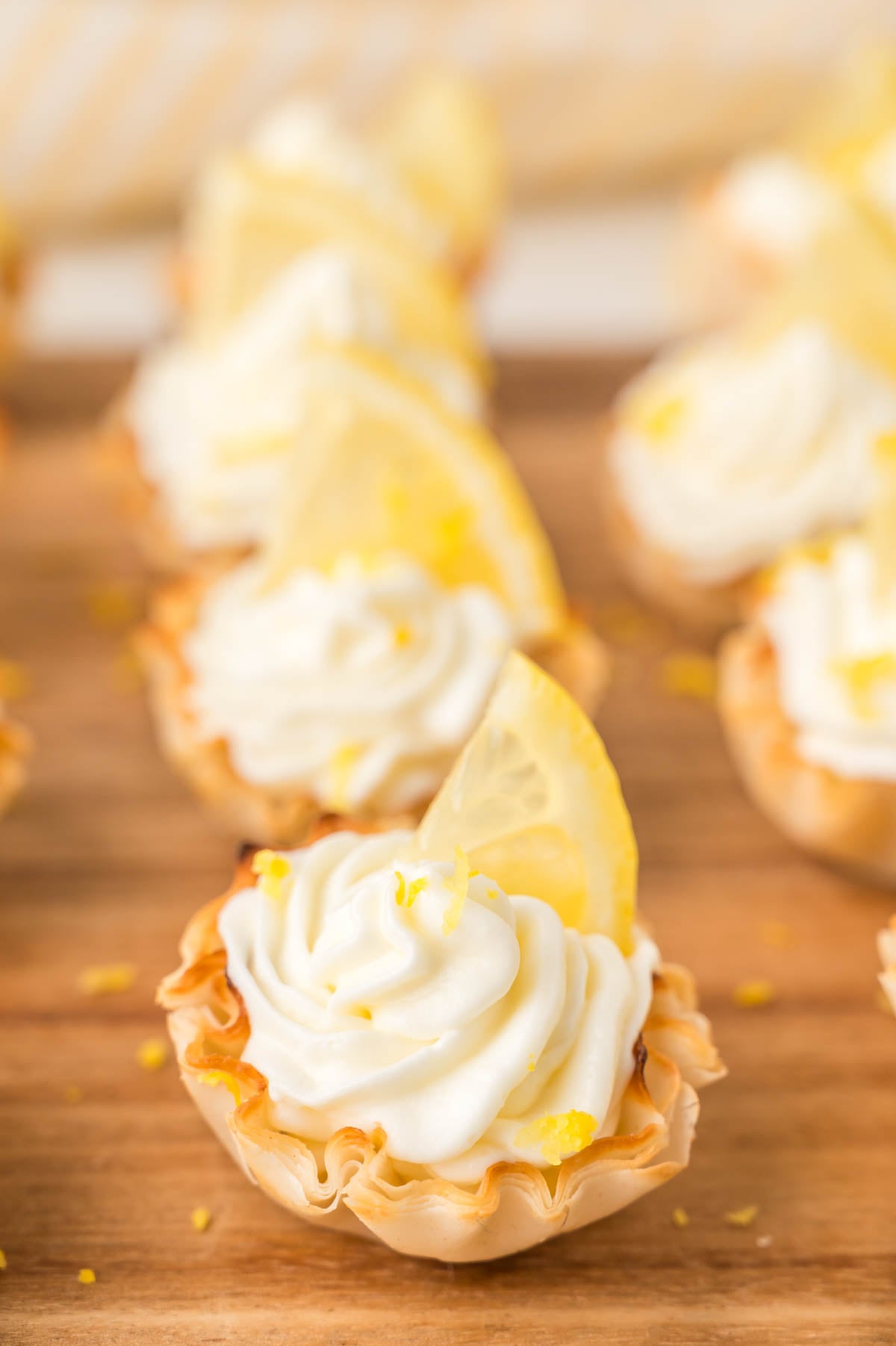 Mini lemon cheesecake bites topped with a small lemon wedge, arranged on a wooden surface.
