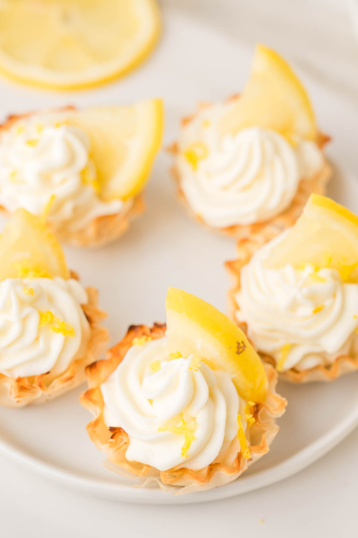 Mini lemon cheesecake bites, each topped with a lemon wedge, arranged on a white plate.