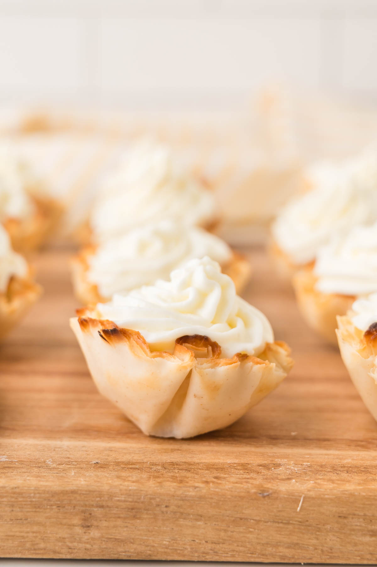 A close-up of mini phyllo pastry cups filled with lemon cheesecake, arranged on a wooden surface.