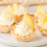 Mini lemon cheesecakes, garnished with lemon slices and lemon zest, arranged on a white plate.