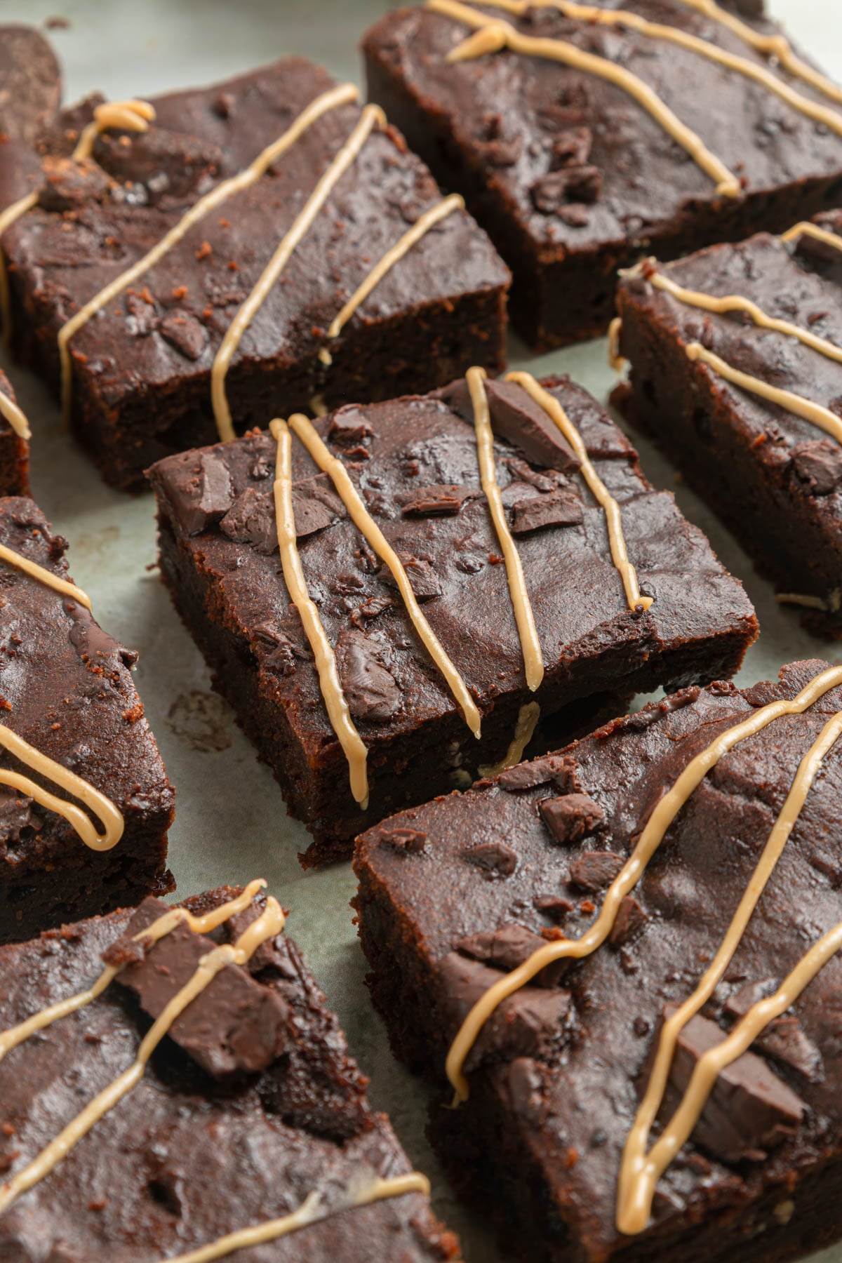 Close-up of several chocolate sweet potato brownies topped with thin drizzles of light-colored icing, arranged in rows on a sheet of parchment paper.