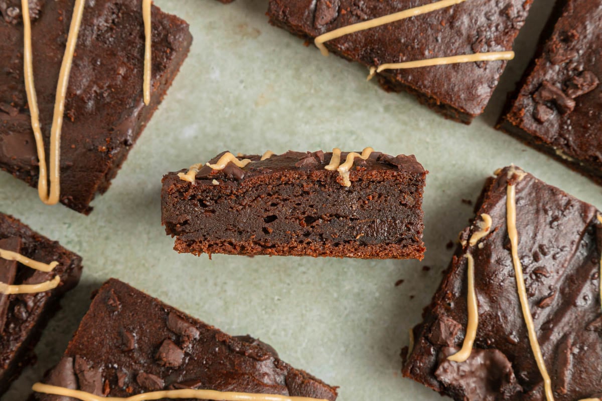 A close-up of sweet potato brownies, one turned on its side to show the fudgy interior, with a drizzle of light-colored icing on top.