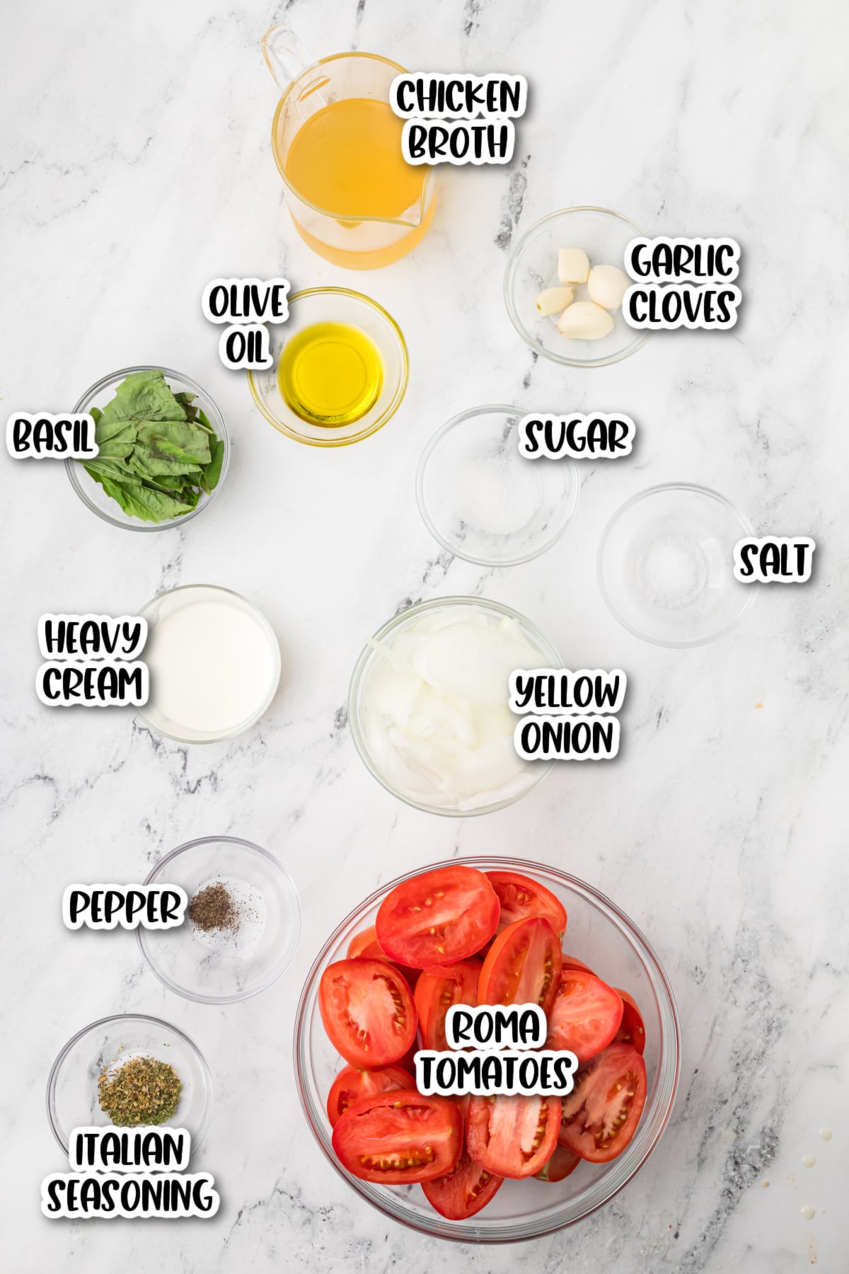 Ingredients for tomato soup arranged on a marble surface, including Roma tomatoes, chicken broth, garlic, onion, basil, olive oil, heavy cream, sugar, salt, pepper, and Italian seasoning.