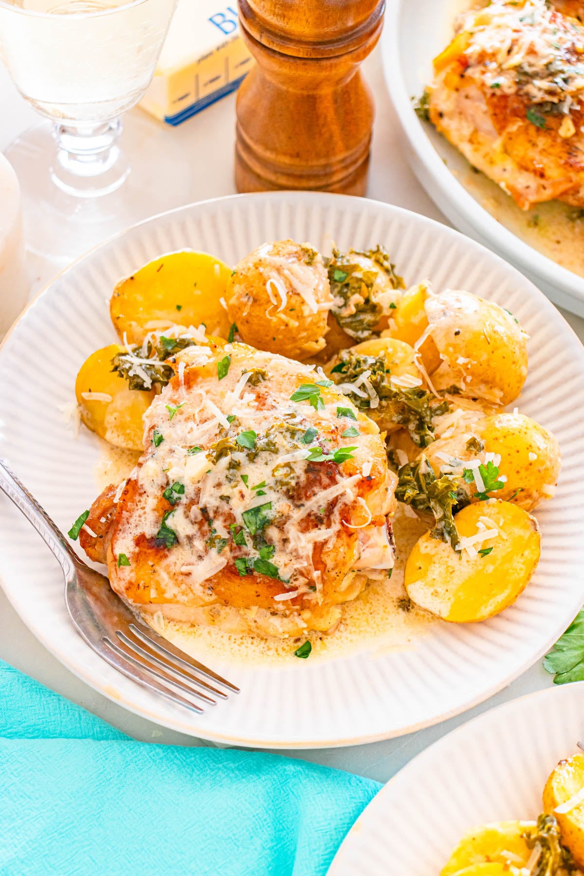 A plate with baked chicken topped with cheese and herbs, served with roasted yellow potatoes, garnished with parsley, and a fork on the side.