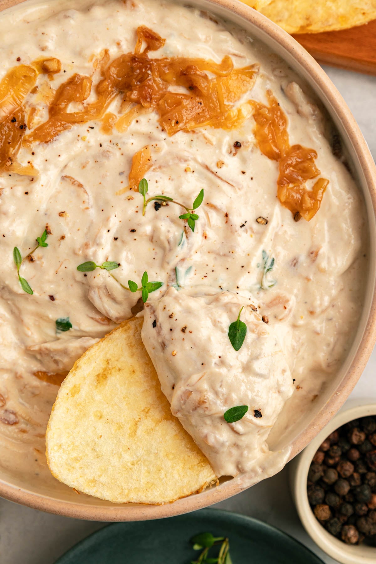 A bowl of creamy dip garnished with caramelized onions and thyme, with a round slice of toasted bread dipped in, seen from above.