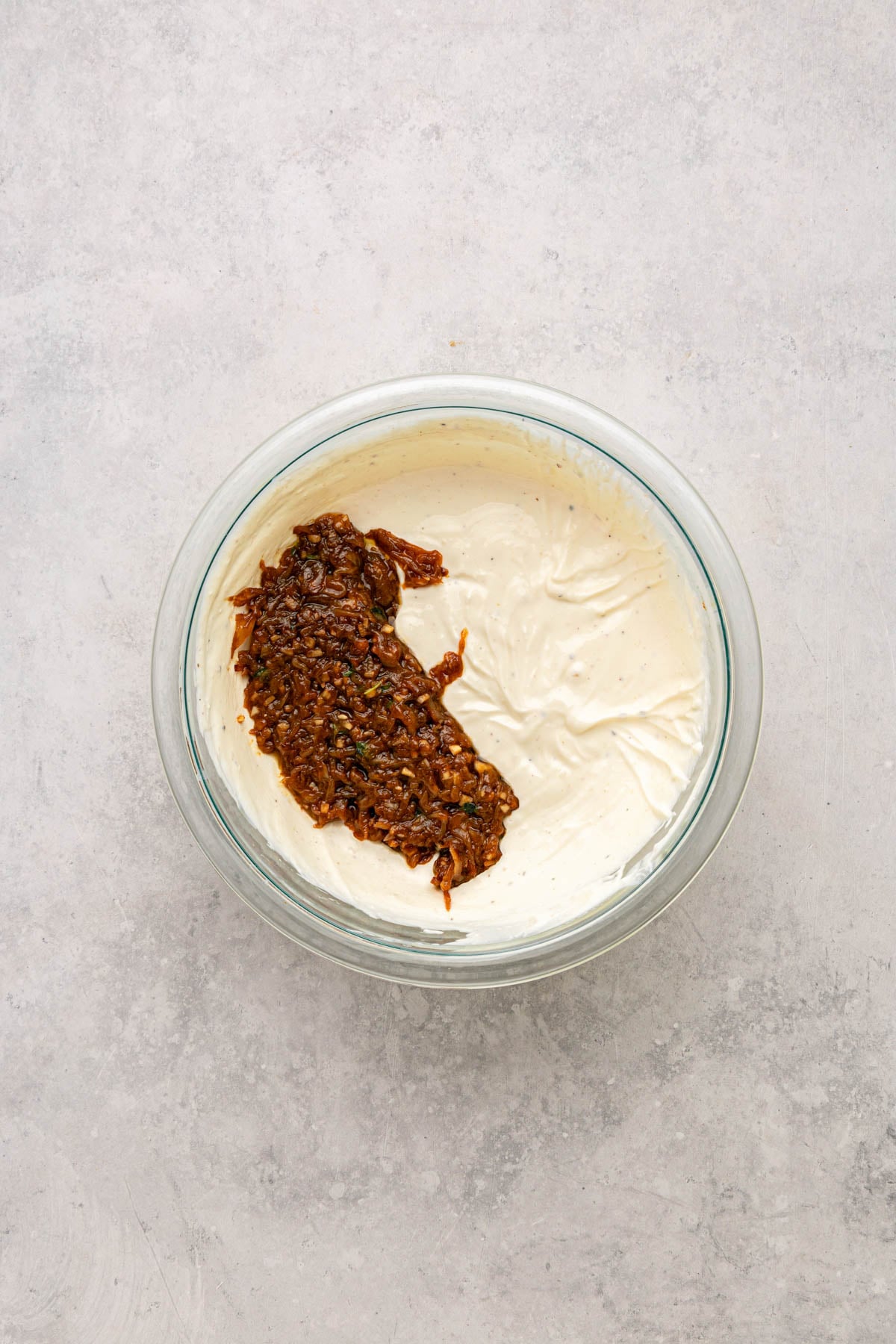 A glass bowl with creamy white mixture and caramelized onions on a gray surface.