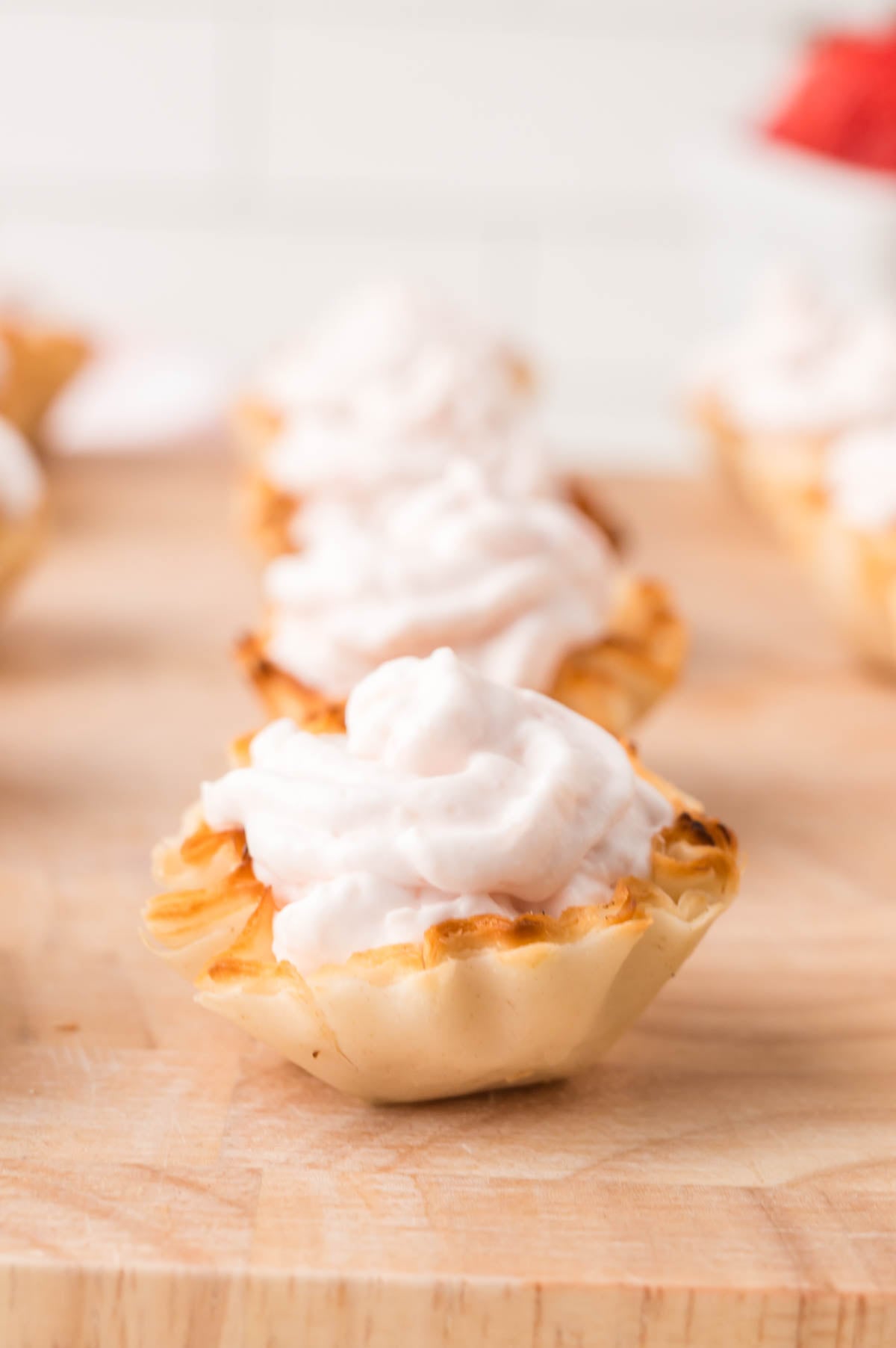 Mini phyllo pastry filled with a creamy, light pink topping, displayed on a wooden surface.