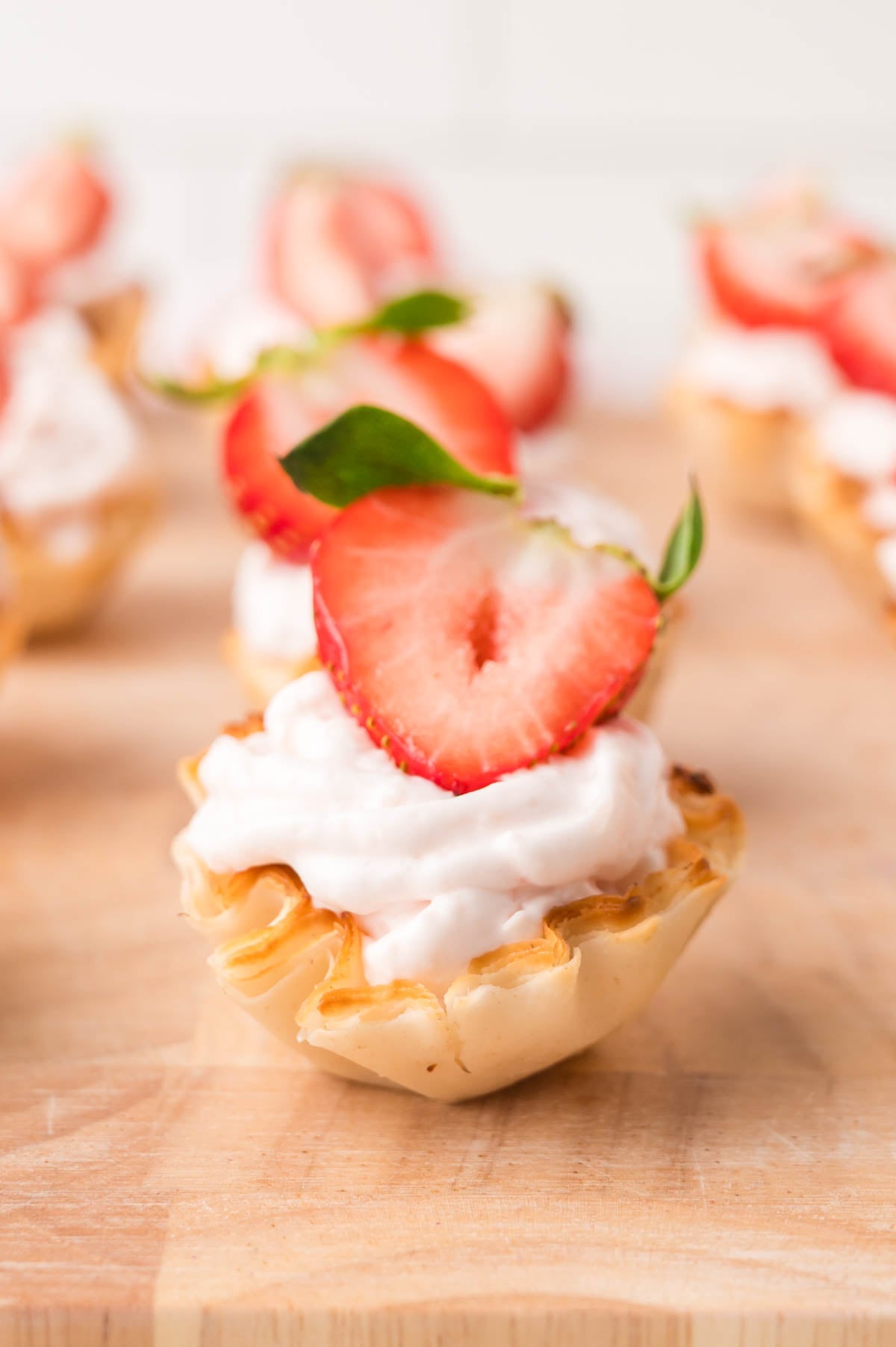 A mini phyllo tart filled with cheesecake and topped with a sliced strawberry, sitting on a wooden surface.