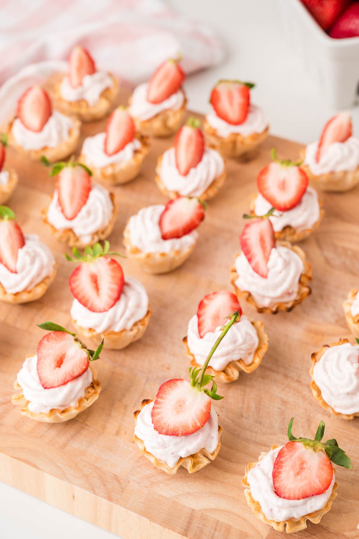 Mini strawberry cheesecake bites topped with sliced strawberries are arranged on a wooden board.