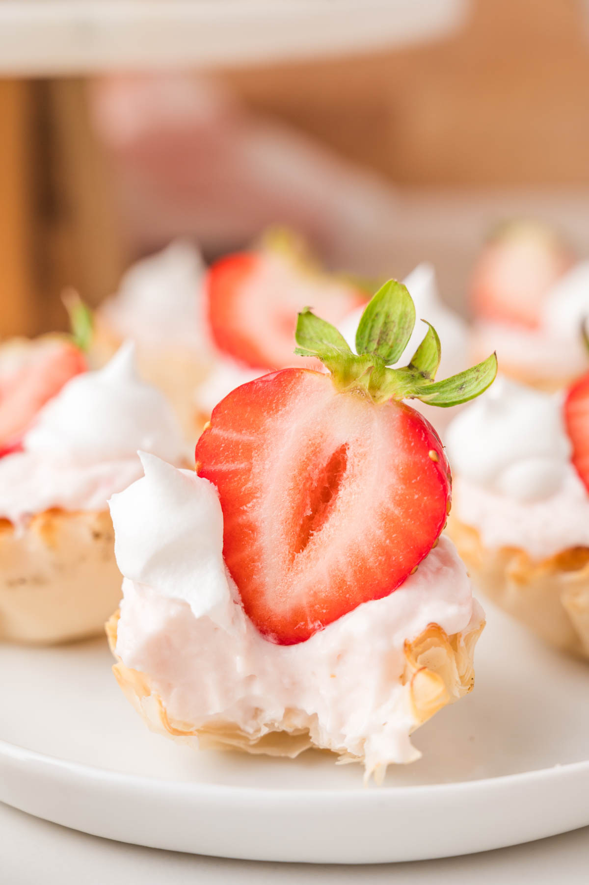 A mini strawberry cheesecake, topped with a halved fresh strawberry and a dollop of whipped cream, on a white plate.