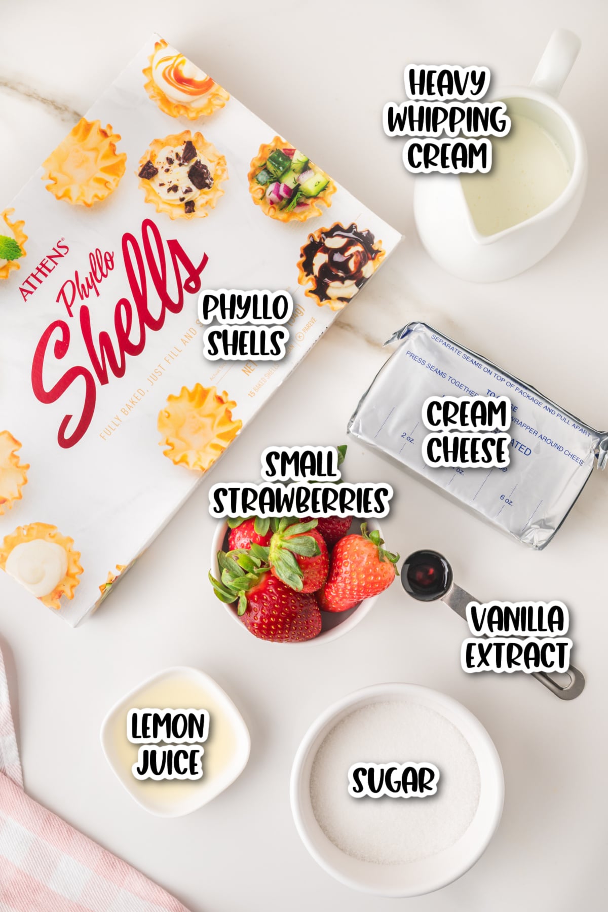 Ingredients on a counter: phyllo shells, cream cheese, heavy whipping cream, small strawberries, vanilla extract, lemon juice, and sugar.