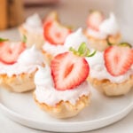 Strawberry cheesecake bites topped with fresh strawberry halves, arranged on a white plate.