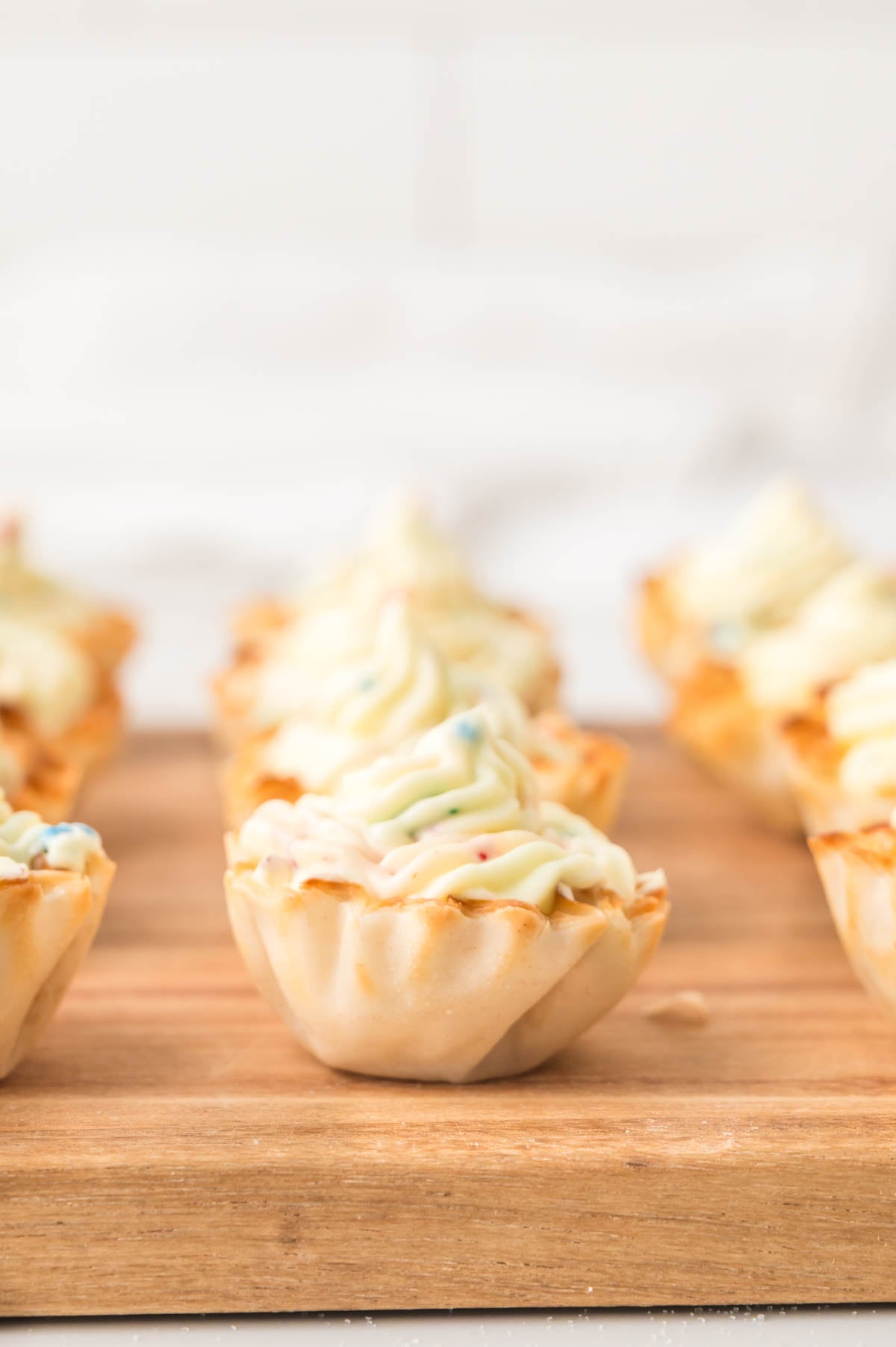 Mini phyllo shells filled with swirled creamy filling are arranged on a wooden board with a blurred background.