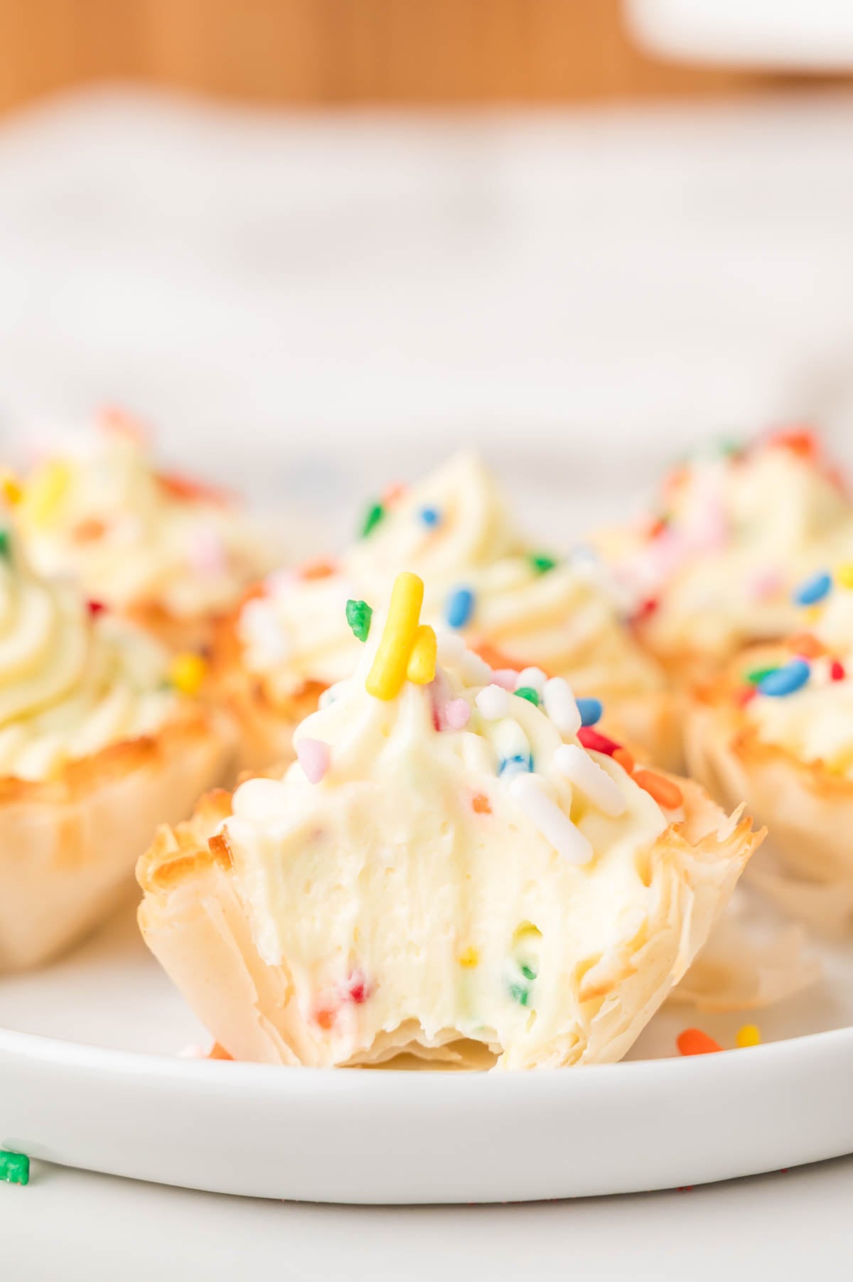 Mini phyllo cup filled with creamy filling and colorful sprinkles, with a bite taken out, displayed on a white plate.