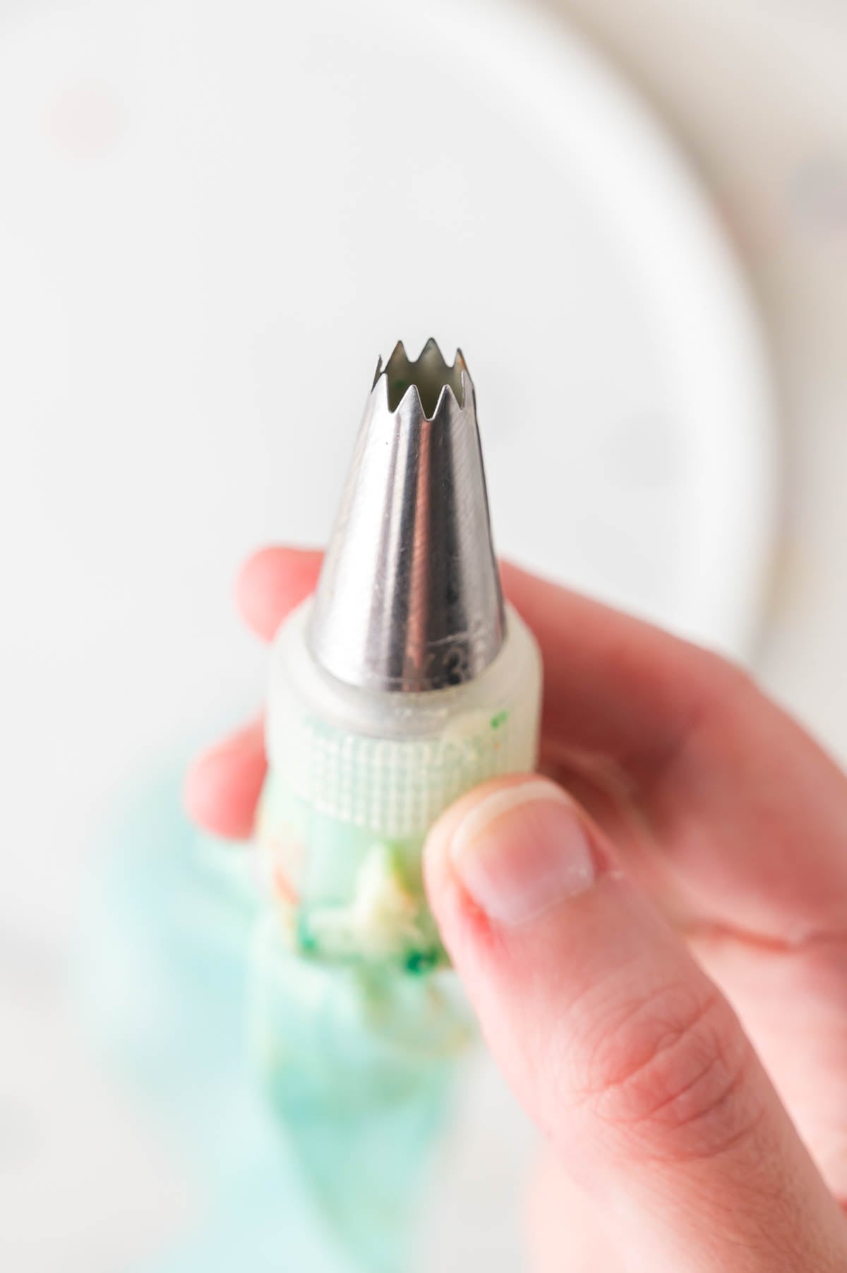 A hand holds a piping bag with a metal star-shaped icing tip, ready for decorating.
