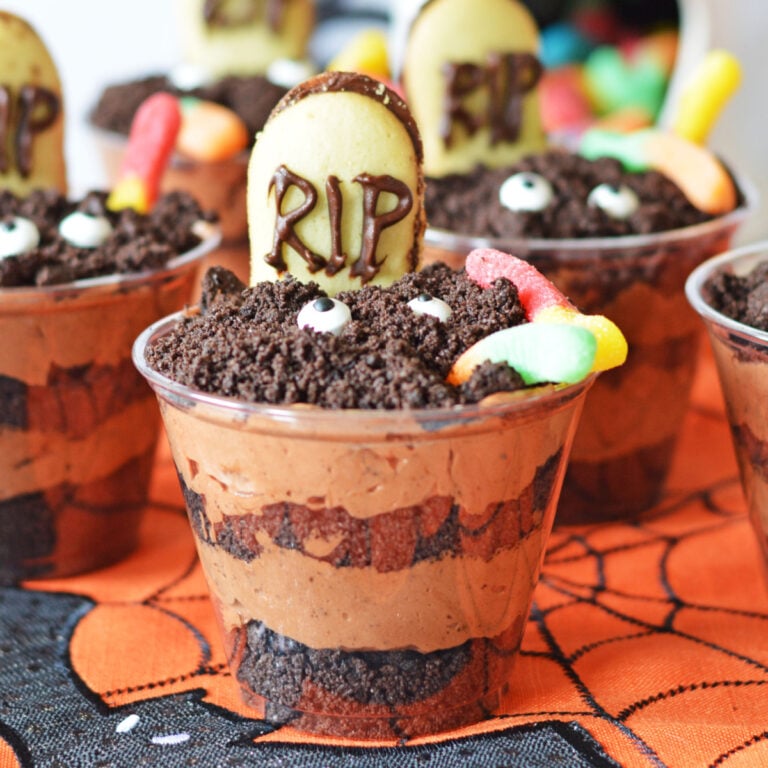 Chocolate pudding cups decorated with crushed cookies, gummy worms, candy eyes, and a cookie marked “RIP,” resembling a Halloween graveyard.