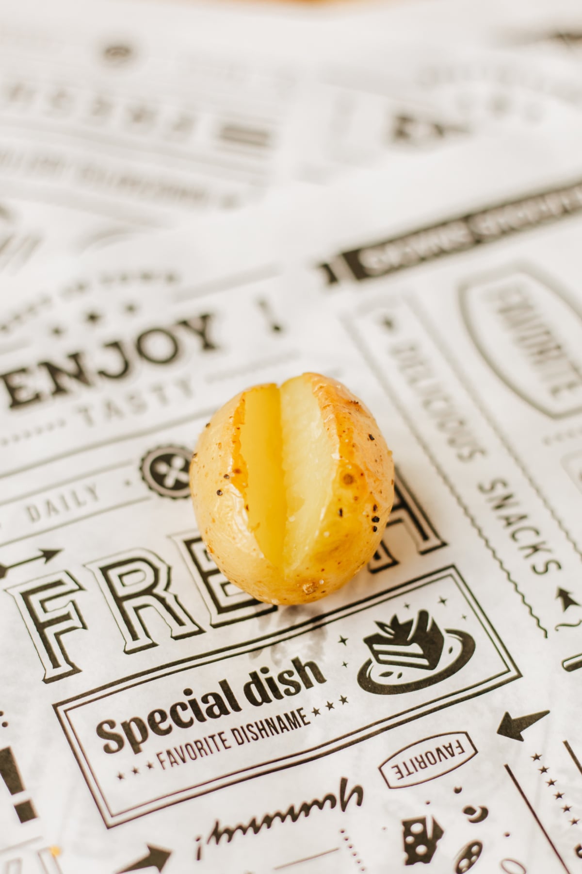 A cooked potato with a split center sits on decorative paper featuring various food-related words and graphics.