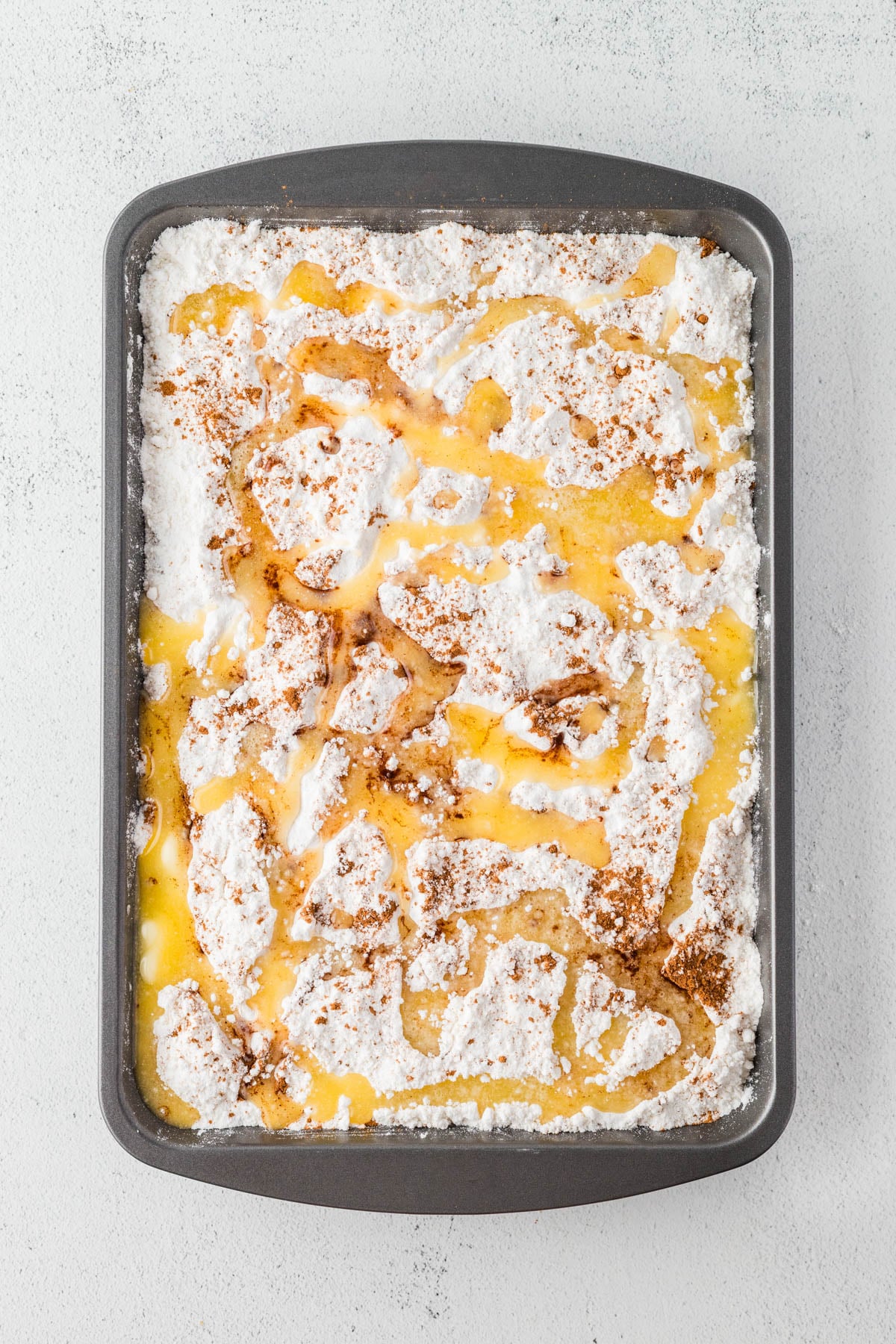 Rectangular baking pan filled with pumpkin mixture topped with cake mix, melted butter, and cinnamon, ready to be baked.