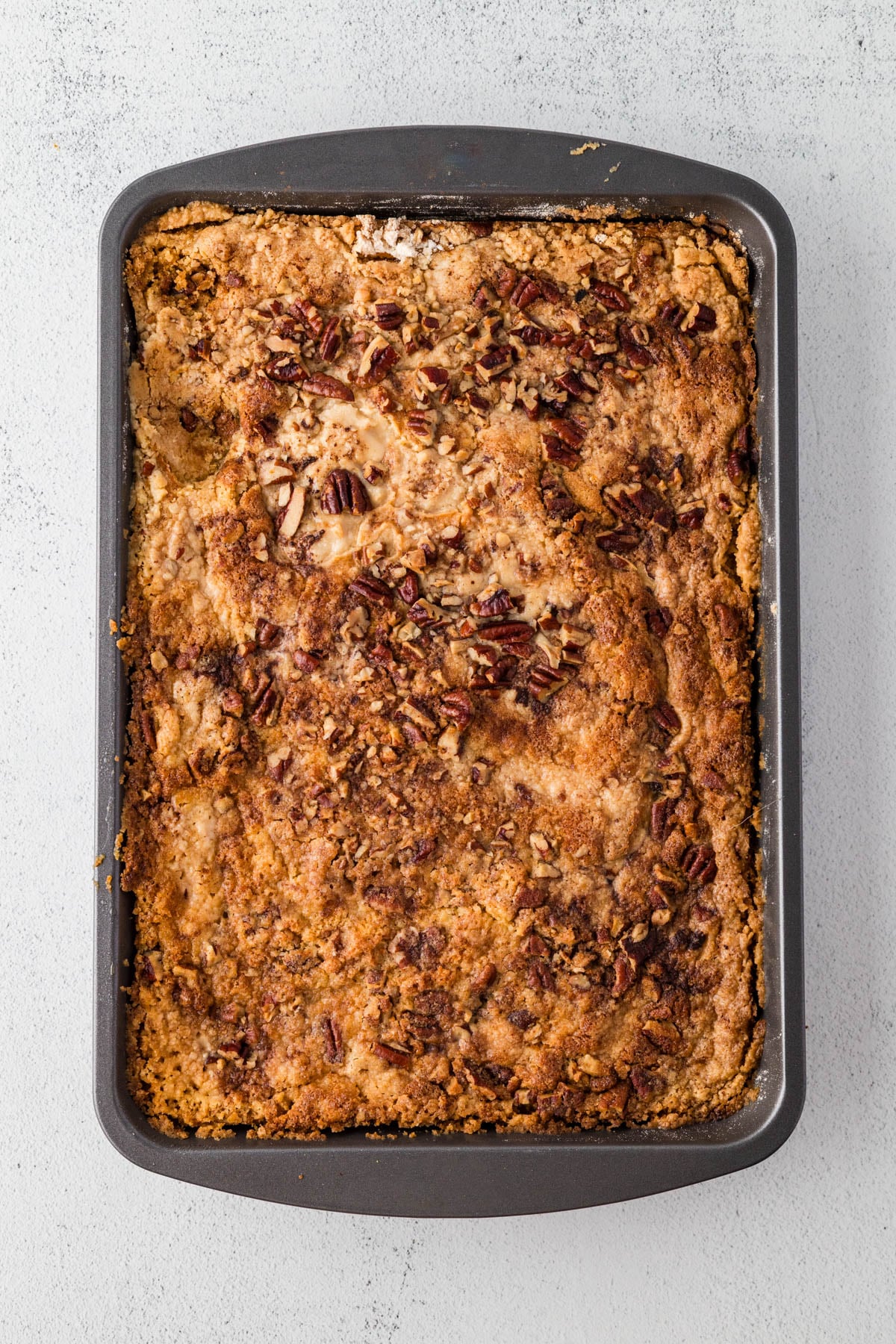 Rectangular baking pan filled with baked dessert topped with chopped pecans and a golden-brown crumbly crust, viewed from above.