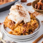 A serving of pecan cobbler topped with a scoop of vanilla ice cream and sprinkled with cinnamon, served on a white plate.