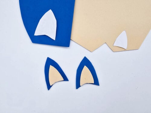 Two pairs of Bluey ear shapes made of overlapping blue and beige craft foam are placed on a white surface.