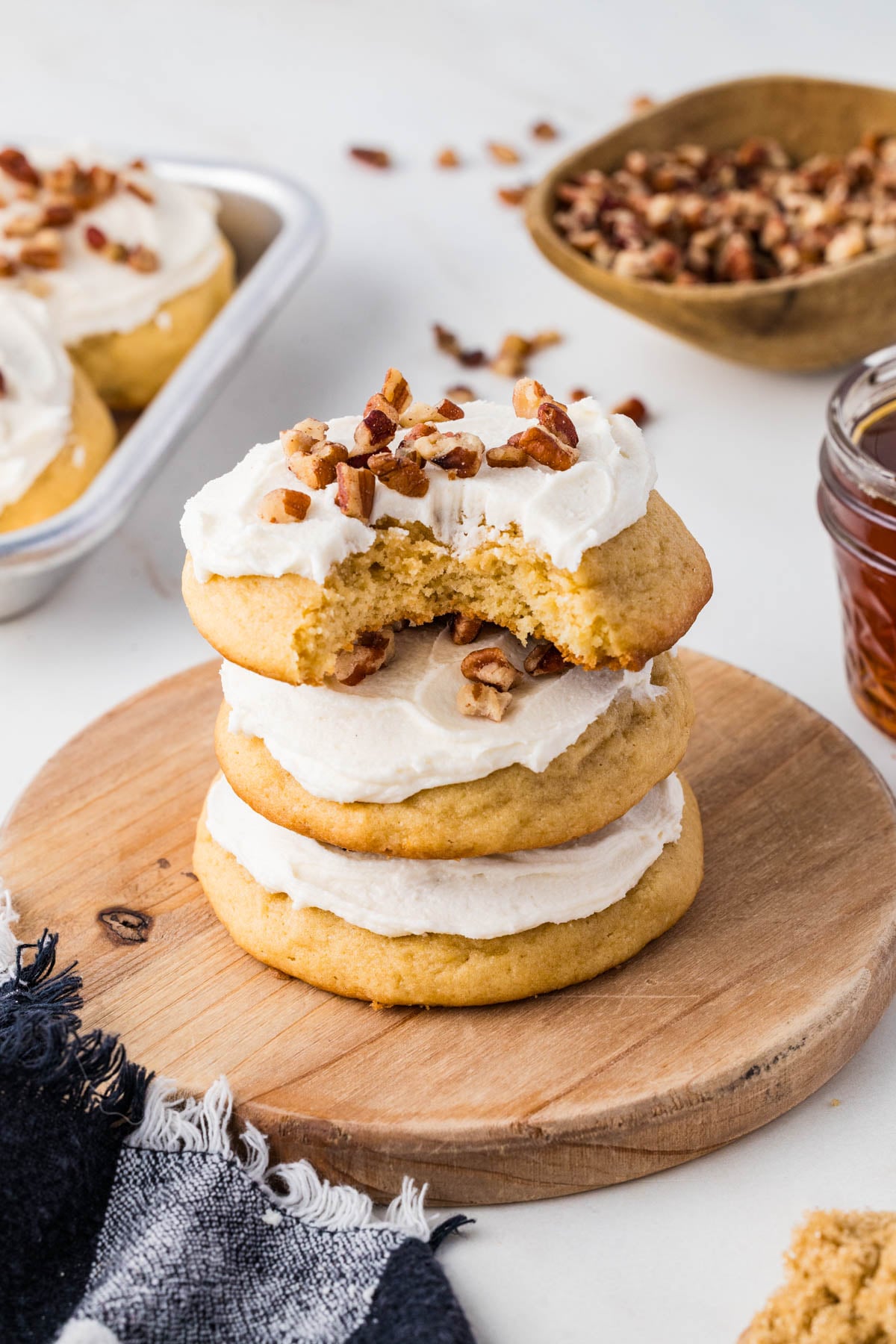 A stack of three frosted cookies topped with pecans, with a bite taken out of the top cookie.