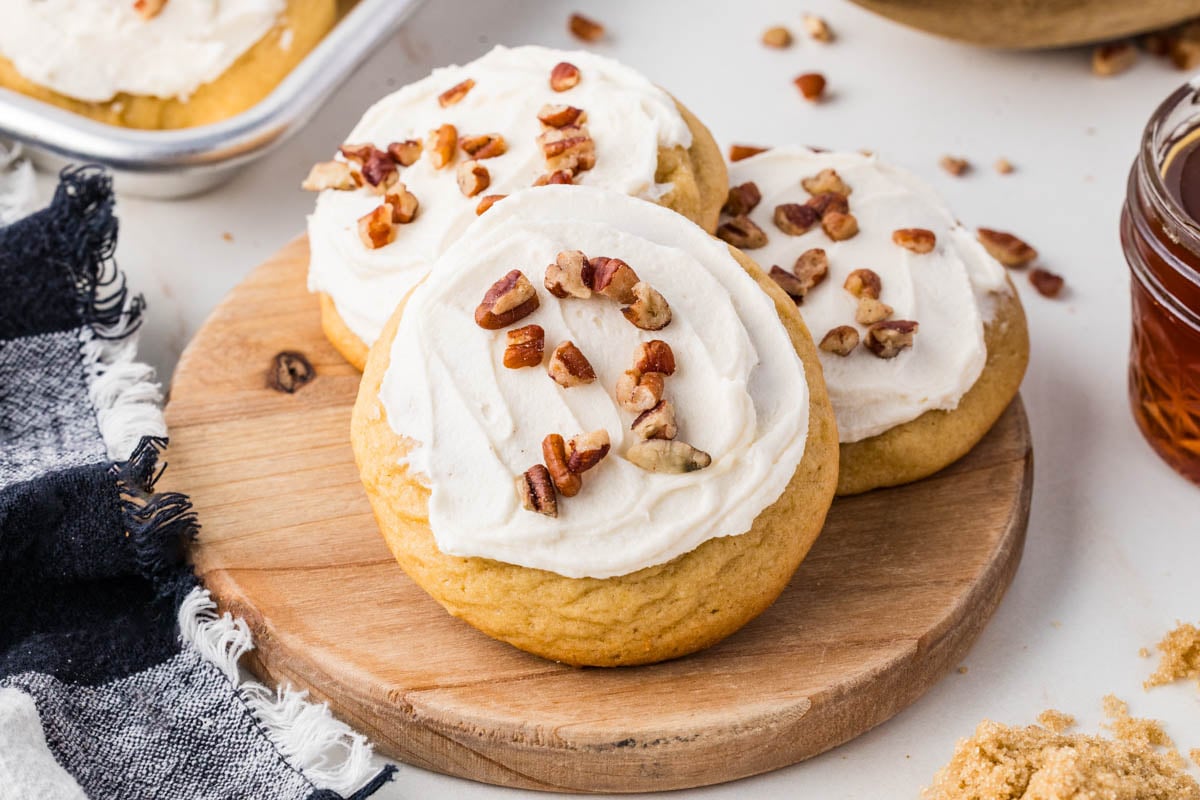 Three cookies topped with white frosting and chopped pecans on a small wooden board.