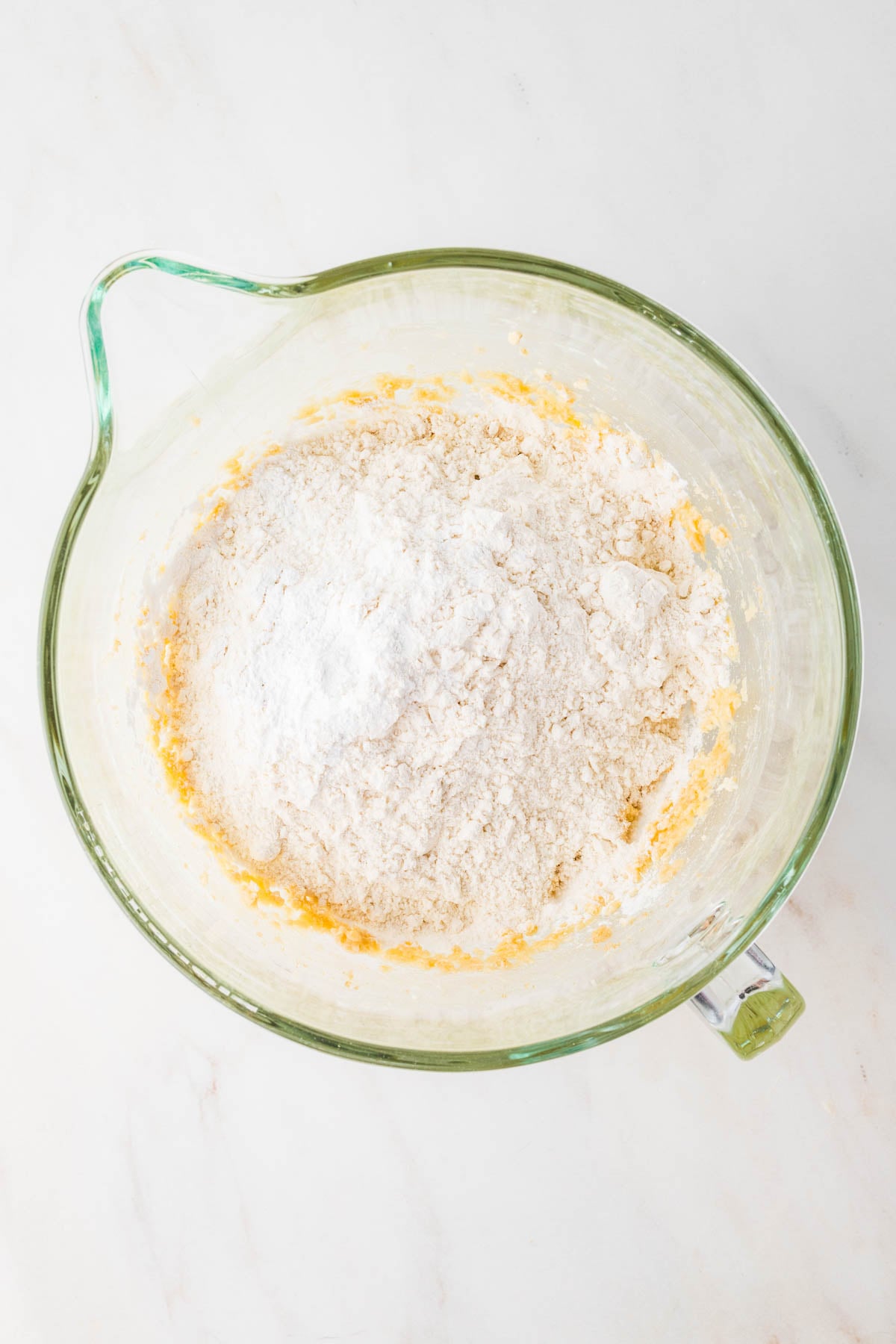 A glass mixing bowl containing flour and other baking ingredients.