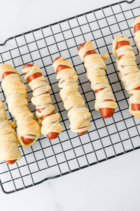 Hot dogs wrapped in strips of dough to resemble mummies on a cooling rack.