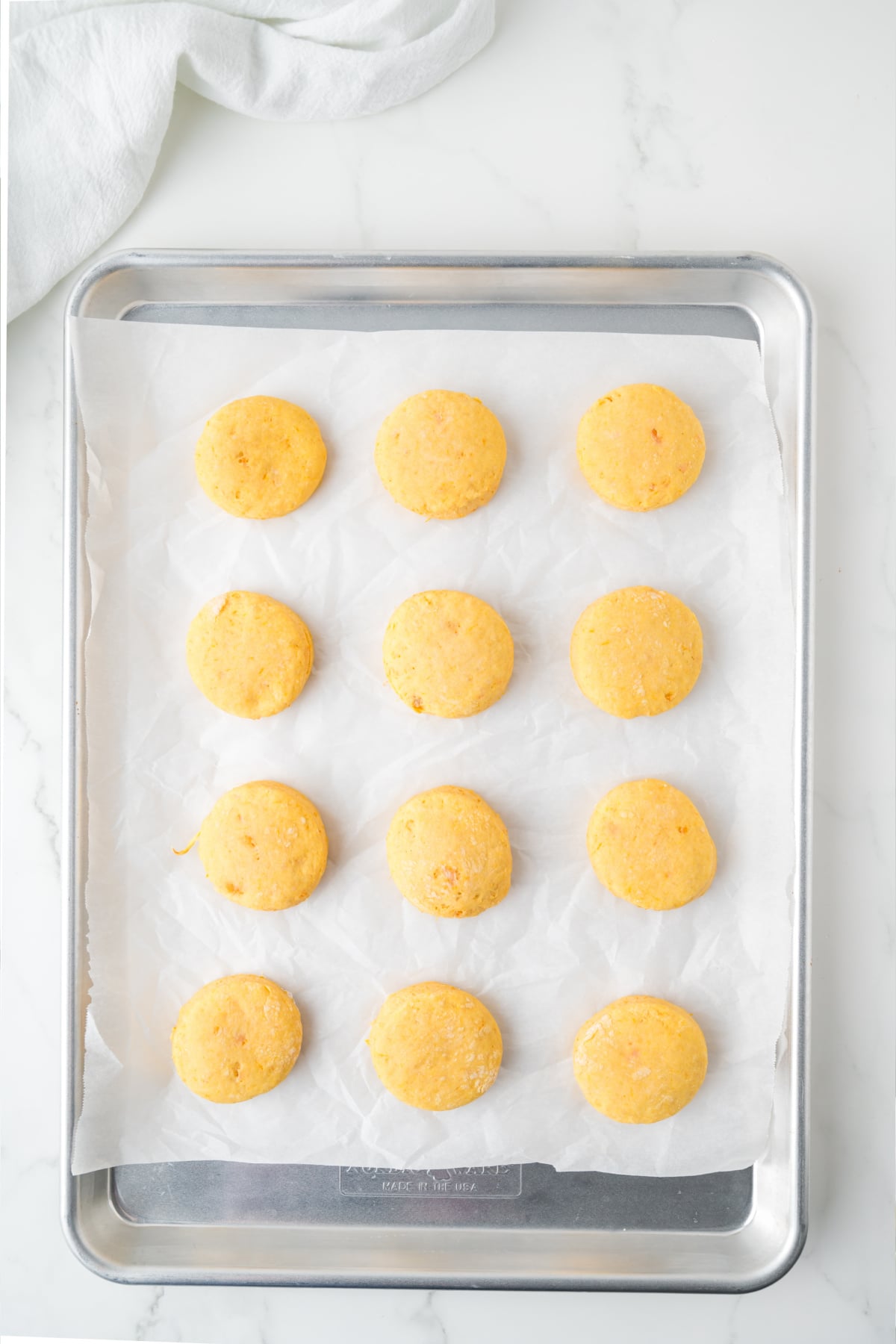 Twelve round, orange dough portions arranged in a grid on a parchment-lined baking sheet.