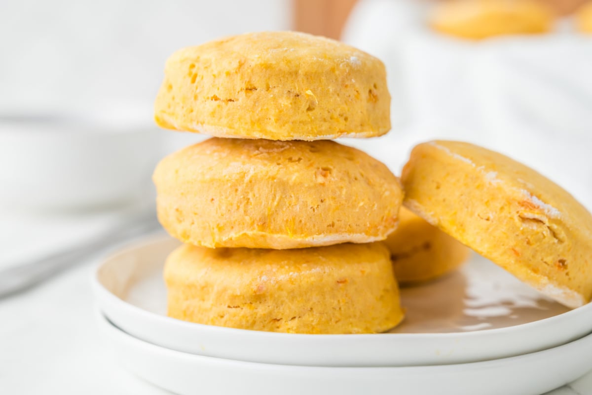 A stack of three sweet potato biscuits on a white plate, with another biscuit resting on the side.