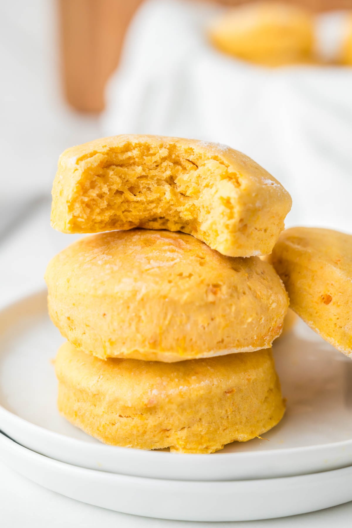 A stack of three golden-orange biscuits on a white plate, with a bite taken out of the top one.