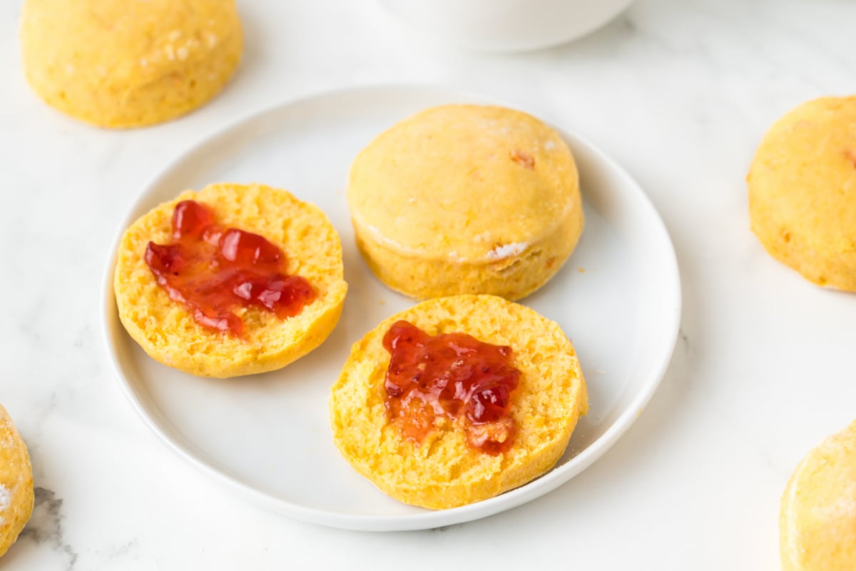 Two split biscuits with strawberry jam on a white plate, surrounded by whole biscuits.